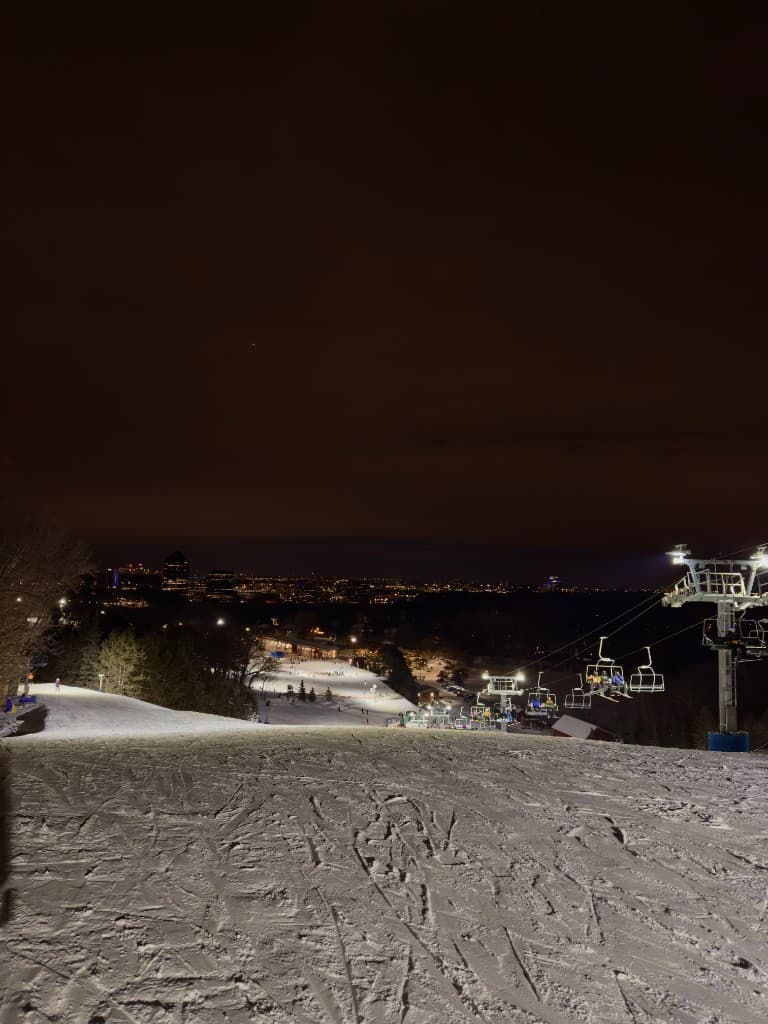 night view down a lit ski slope toward city lights